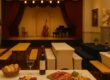 Bierzeltgarnituren mit Hussen im Theater- und Kunstatmosphäre mit Bühne, Instrumenten und Kunstwerken.